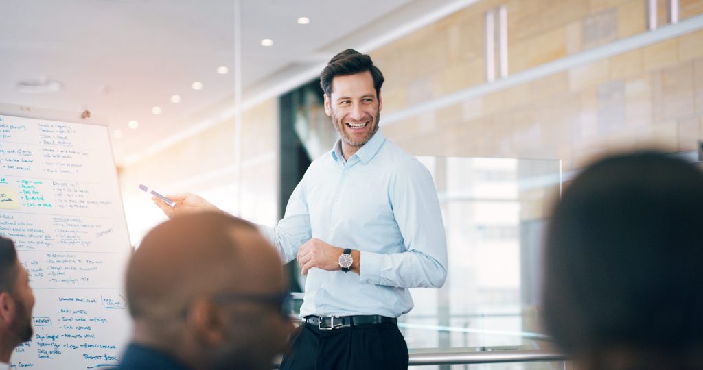 Hes pleased to update them on their progress. a handsome middle aged man giving a presentation during a meeting in a boardroom.